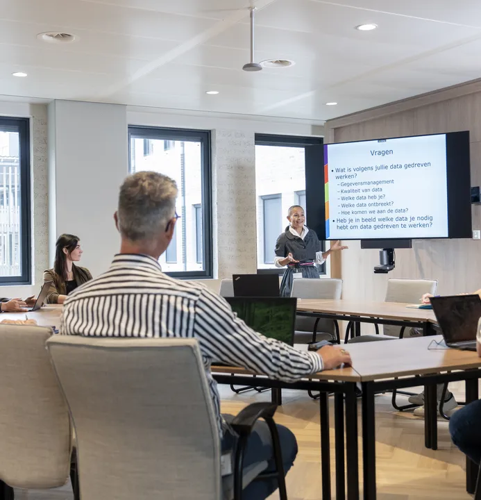Een medewerker van het Huis voor de samenleving vertelt over een presentatie die op het scherm te zi Een medewerker van het Huis voor de samenleving vertelt over een presentatie die op het scherm te zi